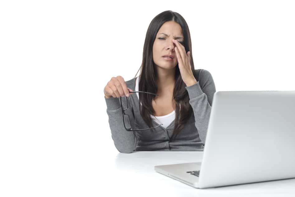 Väsyneeltä näyttävä nainen hieroaa silmiään kannettavan tietokoneen äärellä.