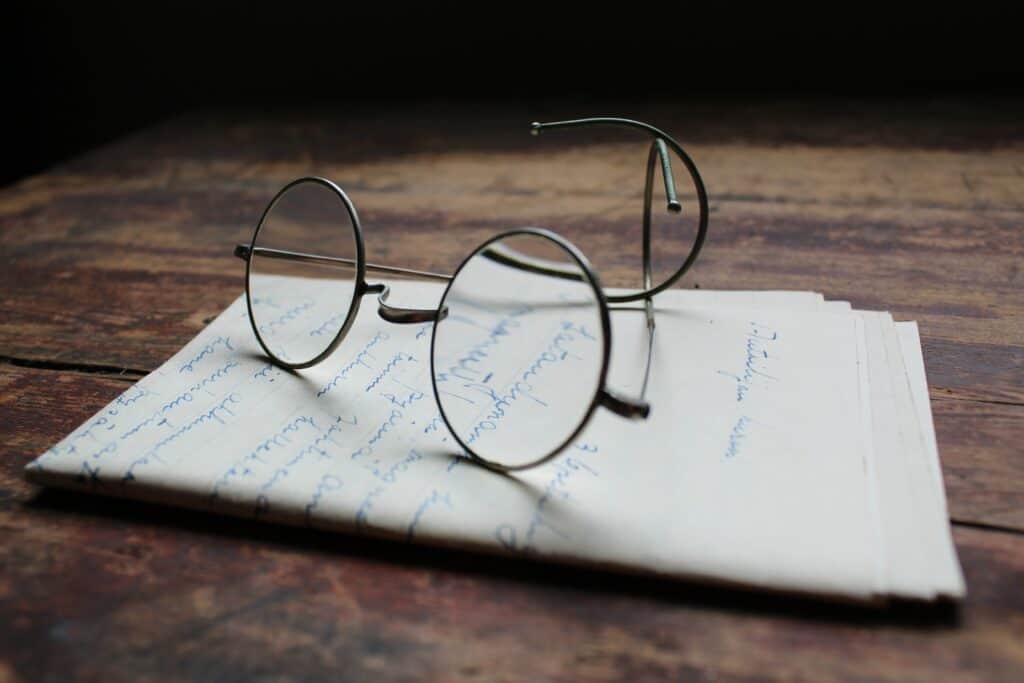 Pyöreäsankaiset silmälasit pöydällä paperipinon päällä.